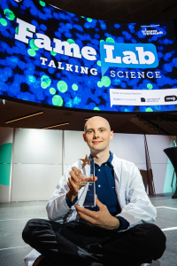 Der Sieger des Vorentscheids von FameLab Germany Maik Gärner sitzt auf der Bühne und hält seinen Pokal in der Hand.