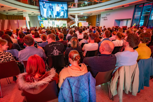 Viele Menschen sitzen in der Wissenswerkstadt vor einer Bühne, die im Hintergrund zu sehen ist.